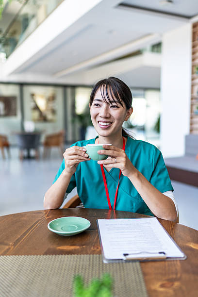 Asian nurse enjoying coffee break, smiling at cafe