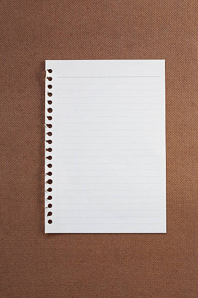 istock Blank lined paper with torn spiral holes on brown background. 2247757432