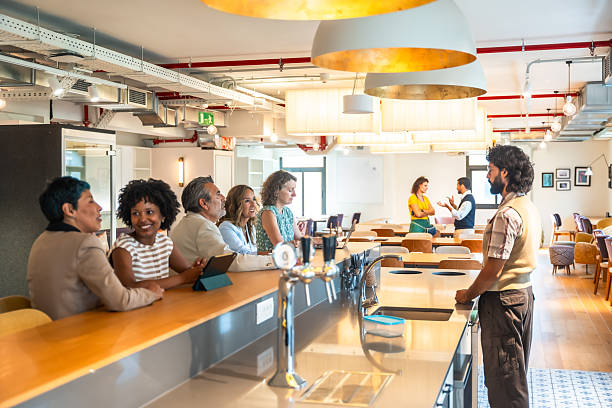 Diverse colleagues from different age groups chatting and collaborating during a relaxed break at the bar area of a modern, upscale coworking office space with bright interiors