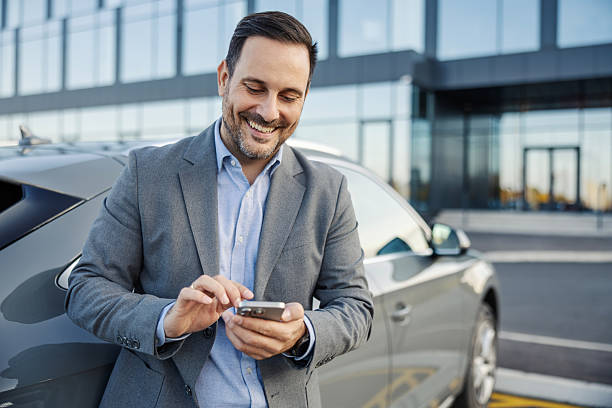 istock Businessman smiling using smart phone leaning on car 2247760294
