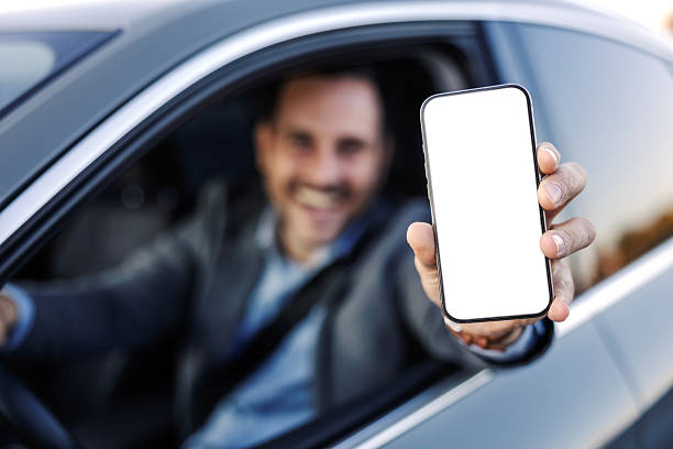 istock Smiling man driving car showing smartphone with blank screen 2247760936