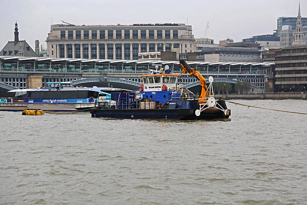 Southbank Boardwalk, London, England, United Kingdom, Europe - November 2nd 2025:  A small group of barges anchored in the River Thames surrounded by autumn-colored trees, with cranes towering above a city construction site in the background.