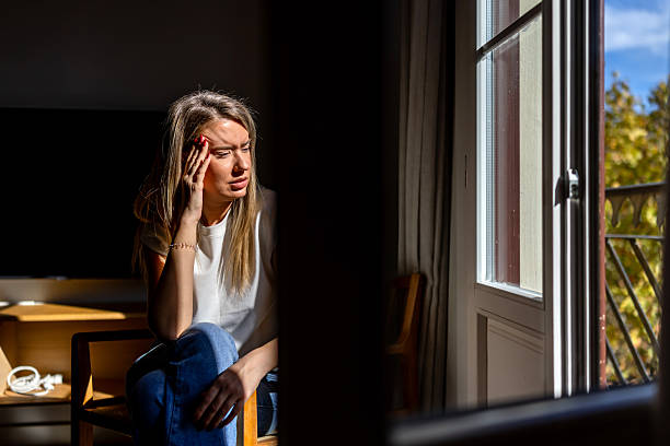 istock Thoughtful Woman Sitting by Open Window in Sunny Room with Dramatic Lighting 2247762248