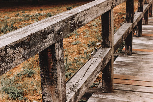 Weathered wooden handrail along a rustic footbridge in a rural setting.