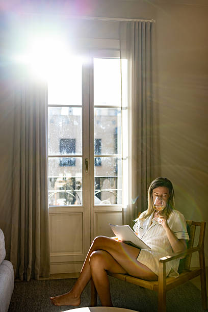 istock Woman Relaxing By Sunlit Window Reading Documents And Drinking Wine In Bright Morning 2247762379