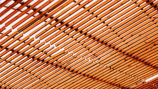 A symmetrical view of wooden roof trusses and beams in a finished attic space, showcasing precise carpentry and natural wood texture. The warm tones and clean lines emphasize structure, craftsmanship, and architectural design. The image reflects sustainable construction and interior detail.