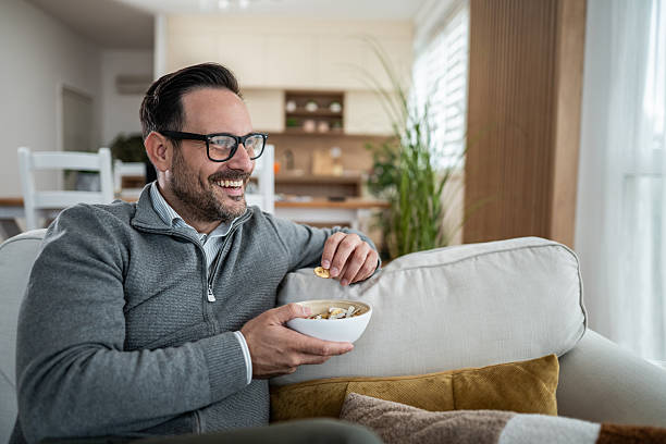 istock Man relaxing on sofa enjoying a snack at home 2247764789