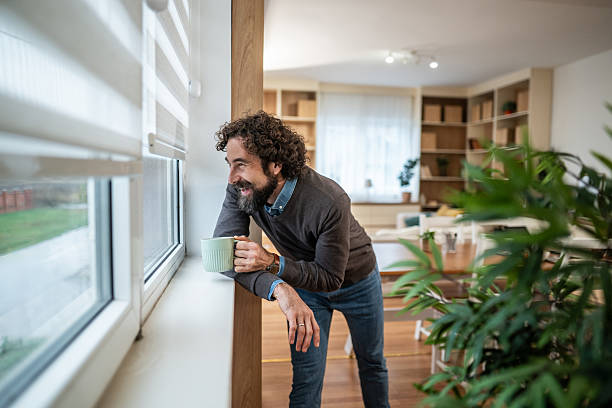 istock Man drinking coffee, smiling and looking out window at home 2247764822
