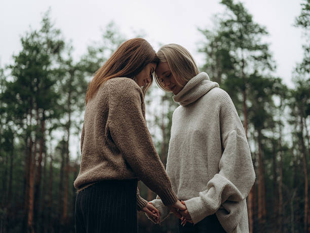 Two young lesbian women touching foreheads holding hands in forest. Emotional close-up portrait showing deep connection, love, and support in LGBT relationship in nature.