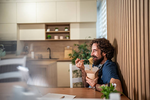 istock Happy man eating takeout noodles in modern kitchen 2247774128