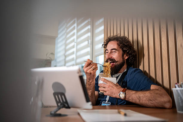 istock Smiling man eating noodles watching digital tablet 2247774244