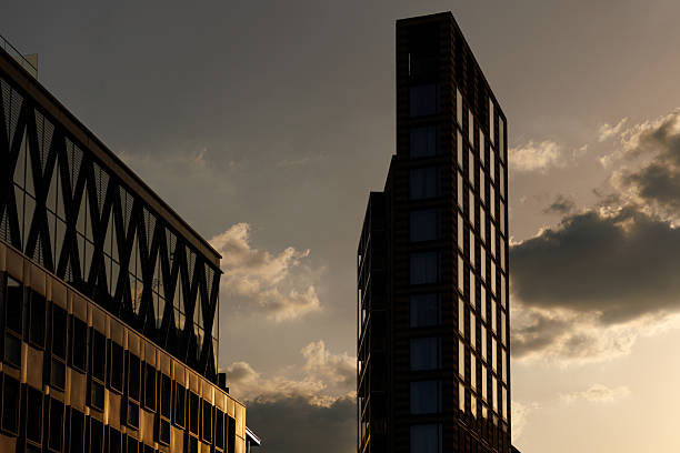 Contemporary office buildings in London are silhouetted against a warm sunset sky.