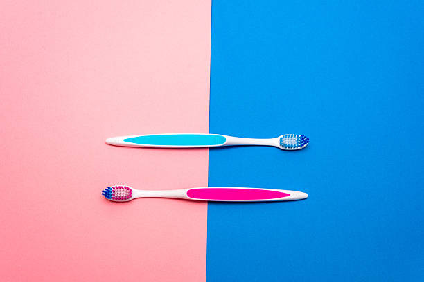 Two vibrant toothbrushes are placed side by side on a split background of pink and blue. The striking colors enhance the visual appeal of daily dental care essentials