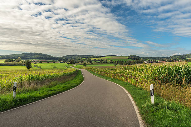 A curved asphalt road leads through cornfields and rolling hills in Baden-Wuerttemberg, Southern Germany.