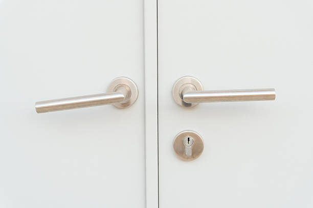 White door panel or door leaf with two silver door grips or handles and separated keyhole is used as background.