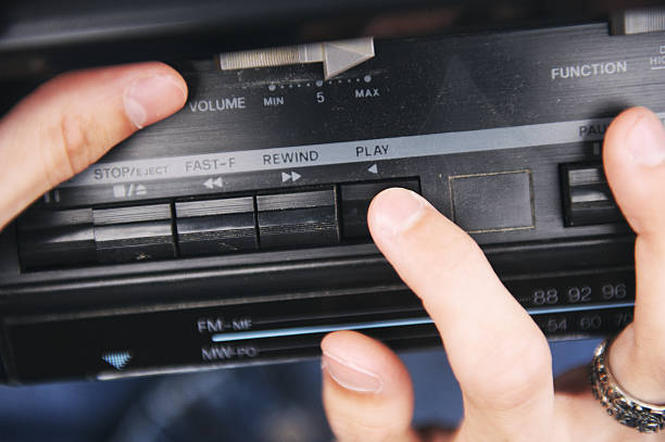 Hands adjust controls on a vintage cassette player to play music.