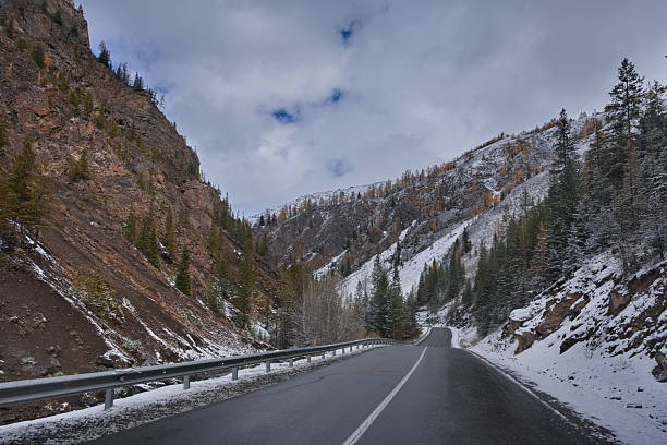 Russia, south of Western Siberia, Altai Mountains. Autumn view of the Aktash-Ulagan highway in the valley of the Chibitka River between the mountains and the snow-covered taiga.