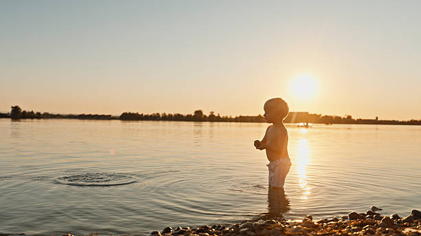 Silhouette of young man standing by lake admiring colorful sky after sunset, enjoy peace and quiet of nature