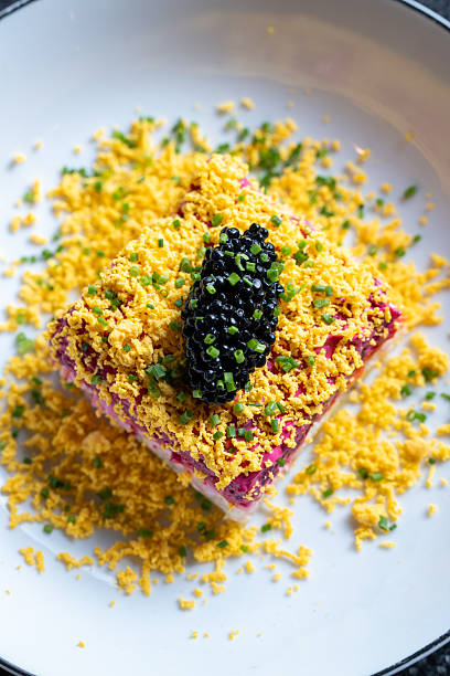 Close-up of a gourmet salad topped with black caviar on a bed of shredded egg garnished with fresh chives on a white plate