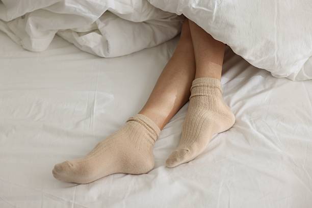 istock Woman in socks on bed with white linens, above view 2247794256