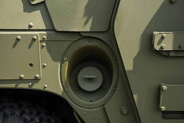 Olive green military utility vehicle parked on a dusty surface, possibly in a military setting Vehicle has vertical grille bars, round headlights, and no visible emblems