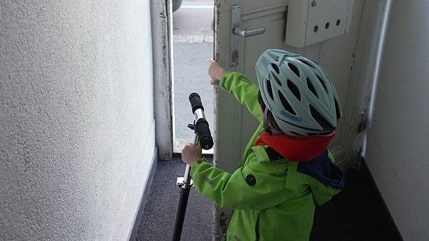 Young child wearing a helmet opens the front door and steps out with a scooter, an adventurous moment filled with excitement and independence, transition from indoors to outdoors