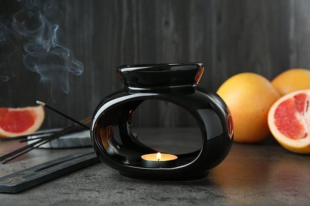 istock Aroma lamp with burning candle, grapefruits and smoldering incense stick on grey textured table against wooden background, closeup 2247798560