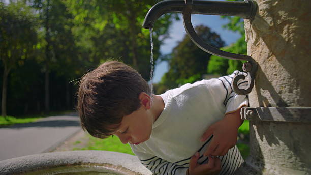 istock Boy close-up drinking from water fountain outdoors, childhood joy and refreshment, summer leisure activity in public park surrounded by trees 2247798608