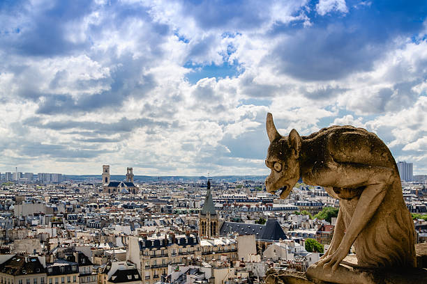 A close-up of a stone gargoyle on the facade of a historic building with a cloudy sky