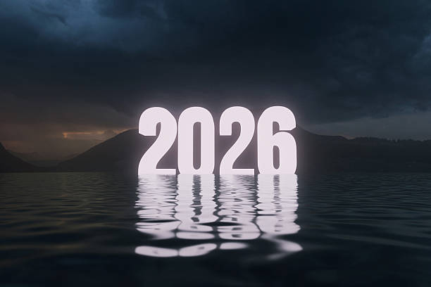 istock Year 2026 illuminated and reflected on dark, rippling water. The dramatic scene features moody clouds and silhouetted mountains in the background, powerful and unknown future. New Year concept 2247799396