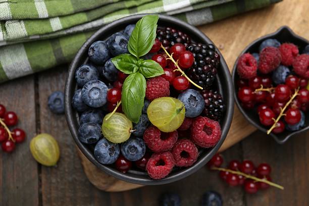 istock Different ripe juicy berries and basil in bowl on wooden table, flat lay 2247799723