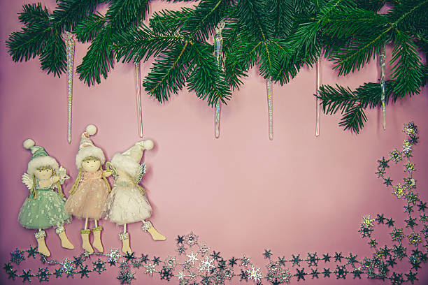 Holiday dolls and fir tree branches arranged creatively on soft pink background. Commercial winter template for gifts, kids promo and seasonal adverts.