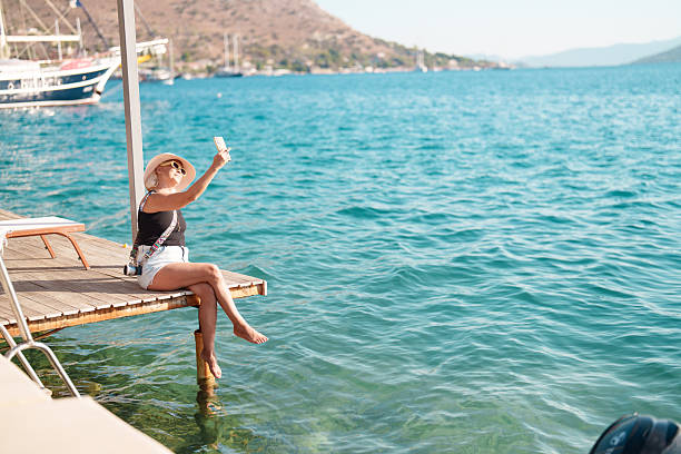 istock A woman sitting on a dock using her smartphone, taking a selfie. 2247800825