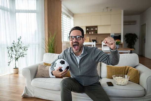 istock Man cheering while watching soccer game at home 2247800876