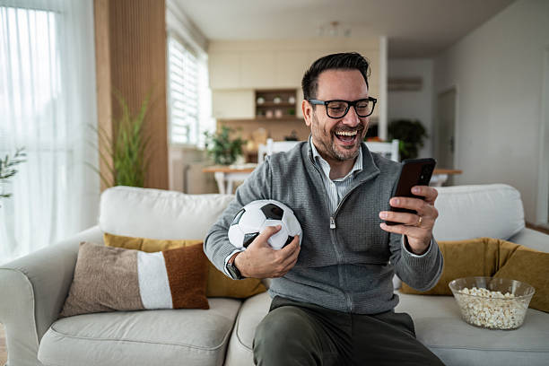 istock Happy man watching soccer on smartphone at home 2247800906