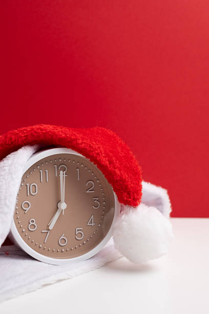 istock Alarm clock covered with santa hat on red and white background. Holiday Countdown. 2247804722