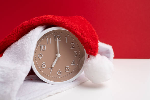 istock Alarm clock covered with santa hat on red and white background. Holiday Countdown. 2247804724