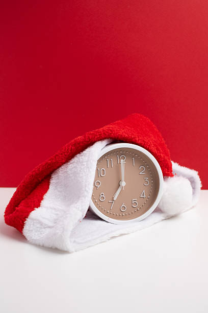 istock Alarm clock covered with santa hat on red and white background. Holiday Countdown. 2247804725