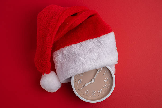 istock Alarm clock covered with santa hat on red and white background. Holiday Countdown. 2247804731
