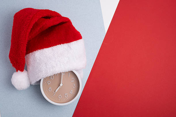 istock Alarm clock covered with santa hat on red and white background. Holiday Countdown. 2247804741