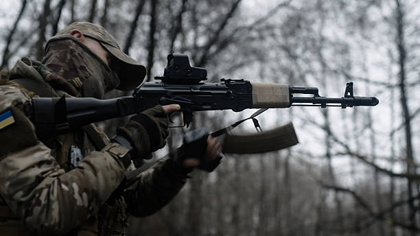 istock Soldier in camouflage uniform with an assault rifle efficiently changes weapon magazine outside. 2247806034