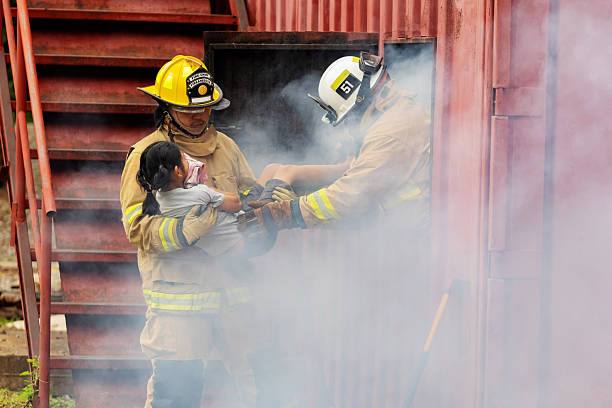 A courageous fireman carries a young girl out of a smoky structure