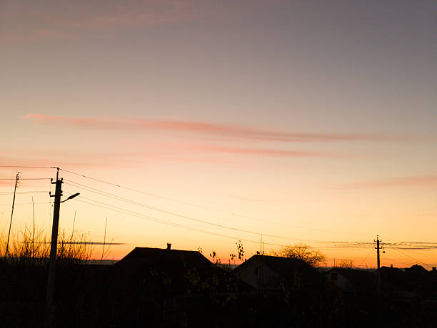 Sunset view with power lines and house roofs.