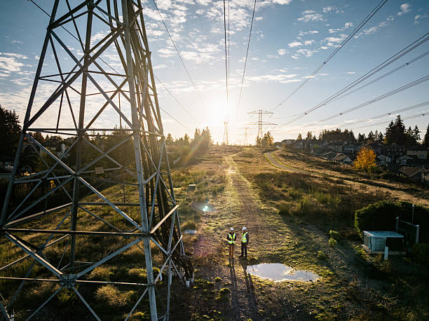 A Caucausan man working as a lineman examining the power grid, utilizing modern technology with a touchscreen tablet.  Hard working maintenance engineer career.  Shot in Washington state.  Drone point of view