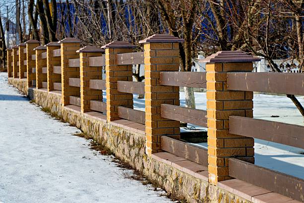 A brick wall with a wooden fence in the snow