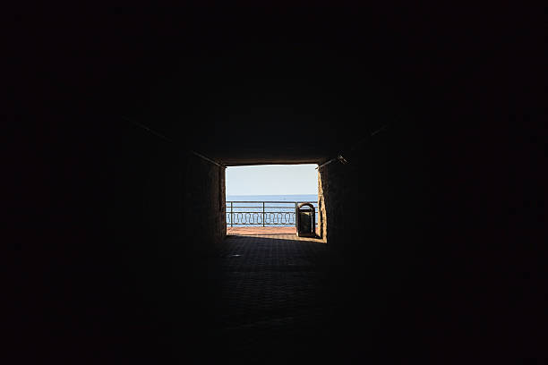 Promenade on a cliff by the sea on a sunny day seen from a covered passage with stone walls in the dark