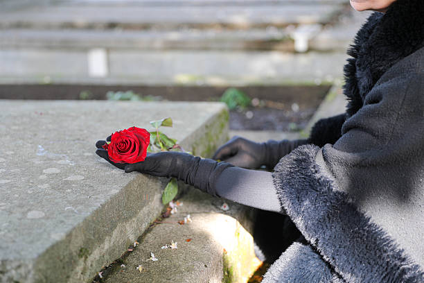 Mourning Elderly Woman Dressed In Black Placing A Red Rose On A Grave In Cemetery As A Symbol Of Grief, Loss, Remembrance And Respect During A Quiet Memorial Moment.