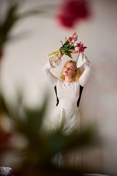 Gentle scene with woman and tulips at home, Tranquil indoor setting showing blonde woman lifting tulips in thoughtful