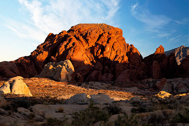 As daylight fades over Valley of Fire State Park, the park's red sandstone formations glow beneath a blue evening sky. The waning sunlight highlights the desert landscape, balancing warm stone against a cooling sky. The scene captured the quiet transition between day and night in one of Nevada's most striking desert environments.