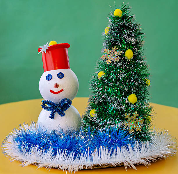istock A snowman decorated with a red hat and blue scarf is placed next to a Christmas tree with blue and white decorations 2247830109